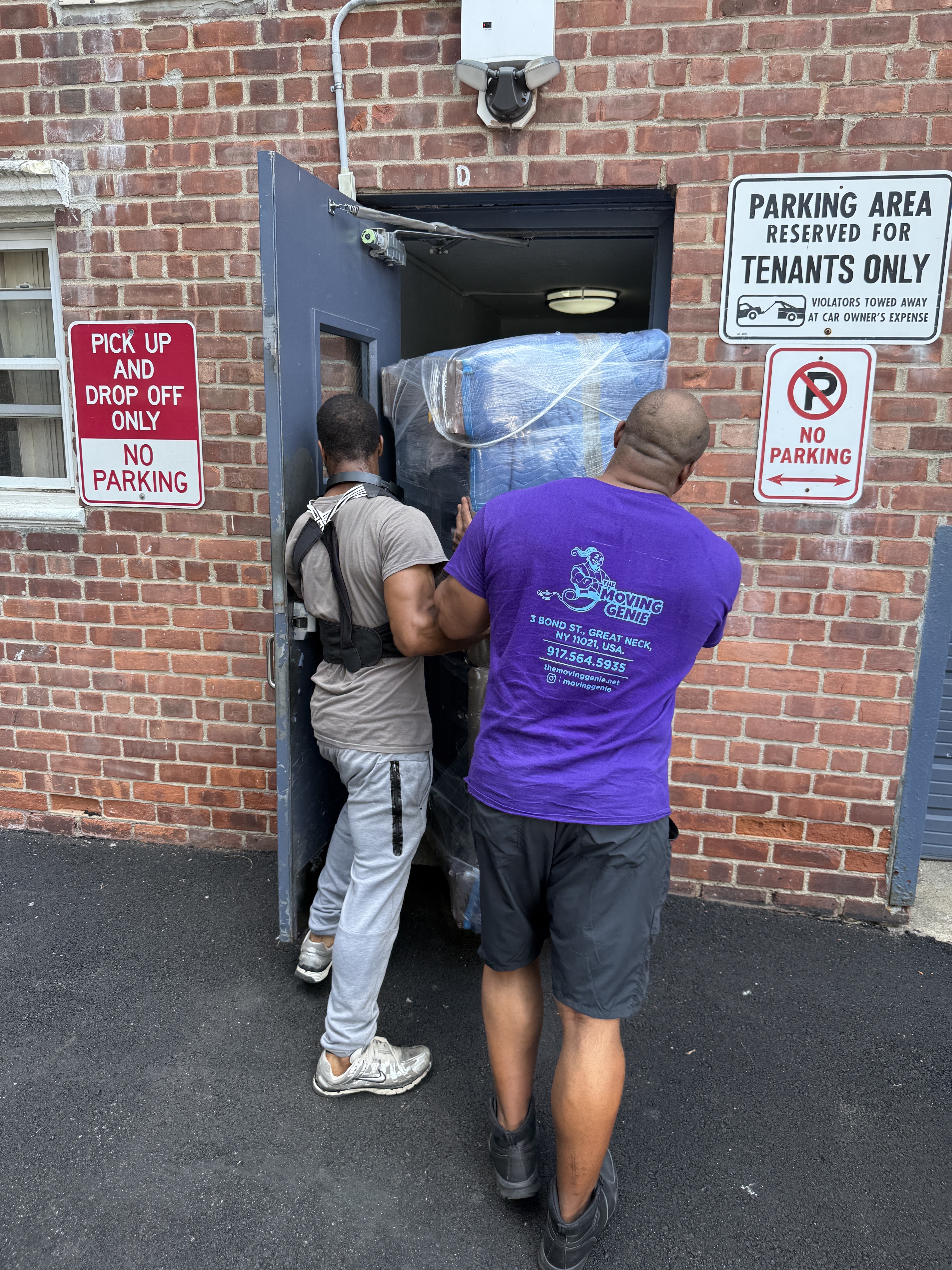 Two Moving Genie movers carefully carrying a wrapped item through a Great Neck building doorway