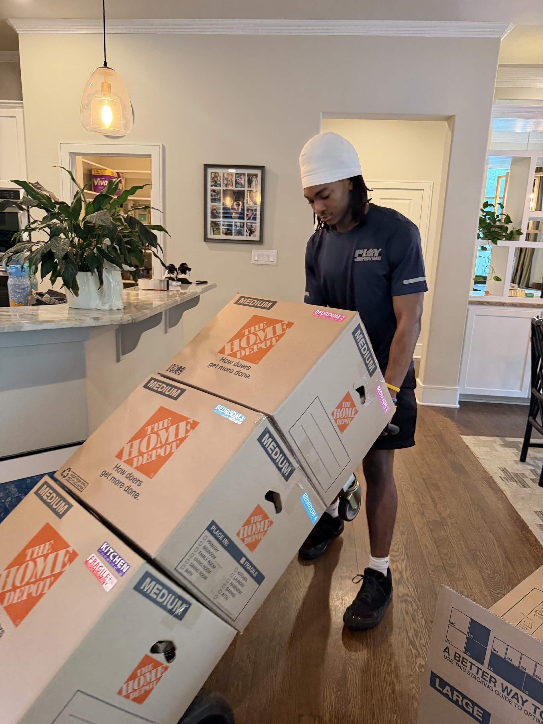 A Playhouse Moving crew member wheeling a stack of labeled Home Depot boxes on a dolly through an Austin home
