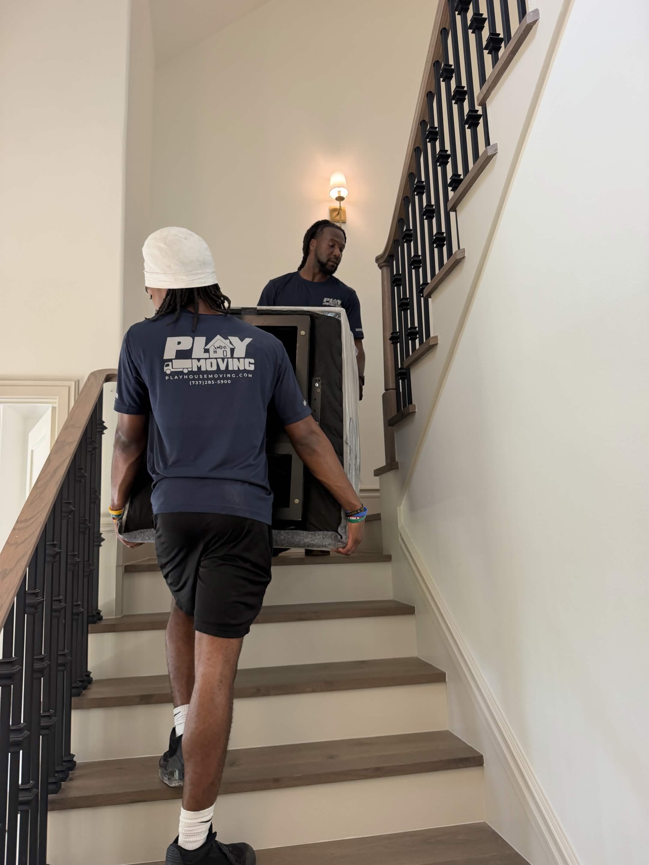 Two movers carefully carrying a wrapped item up a residential staircase in an Austin-area home